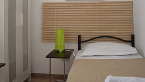 A bedroom with a bed, a small table with a green object, a wooden headboard, and a wall-mounted picture of a flower.