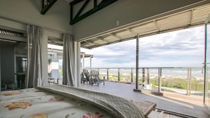 Quarto com uma cama grande, varanda com vista para a praia e área de jantar com cadeiras.