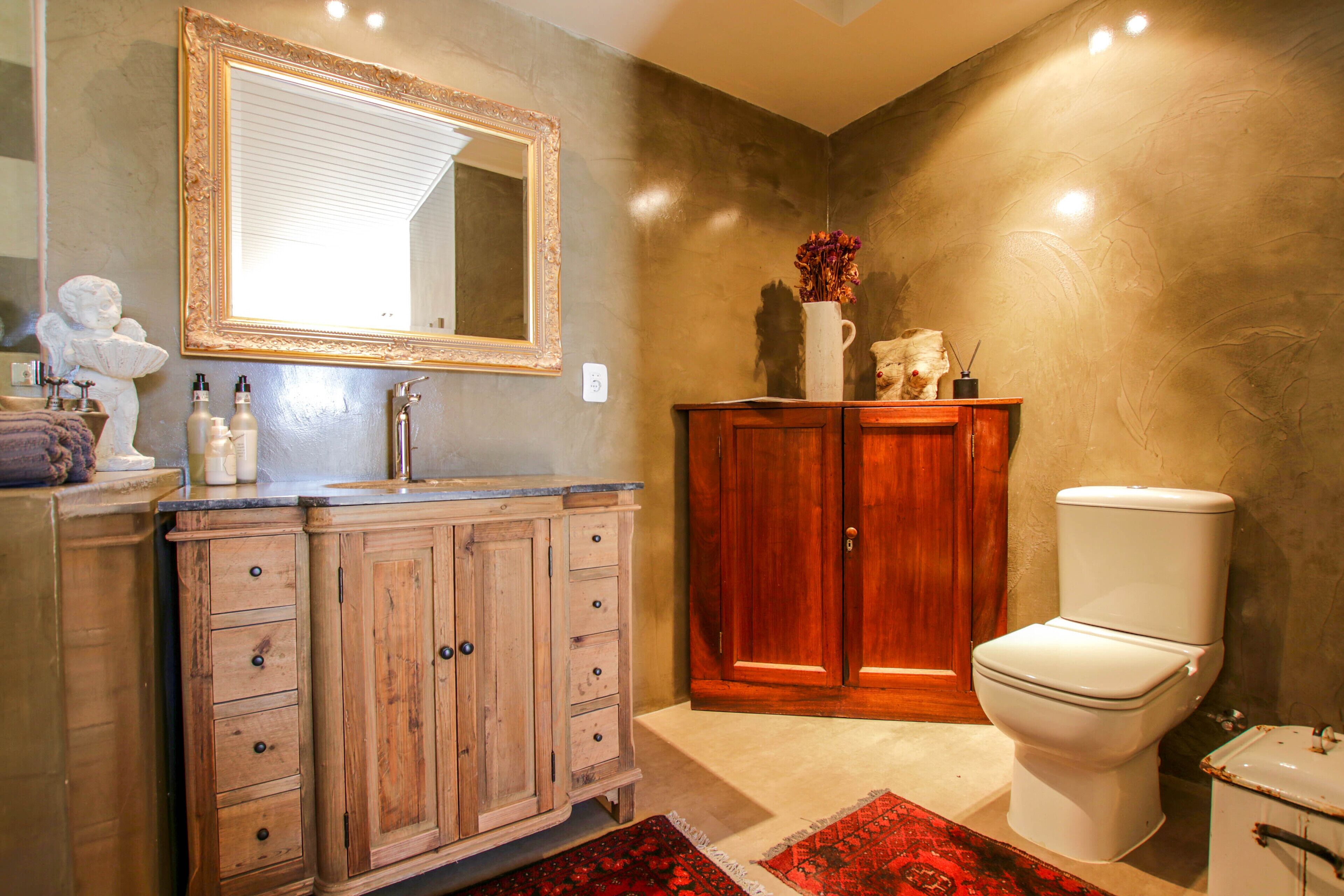 Une salle de bain avec un meuble-lavabo en bois, un grand miroir, des toilettes et un tapis rouge.
