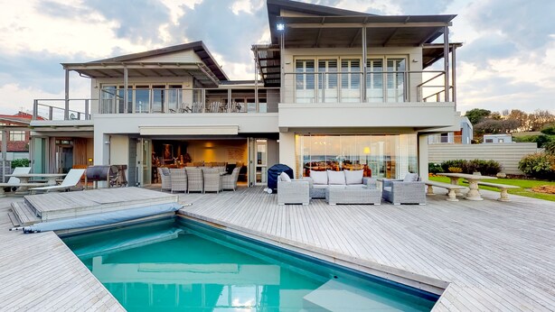 Uma casa moderna de dois andares com piscina, móveis de exterior e um espaço de varanda.