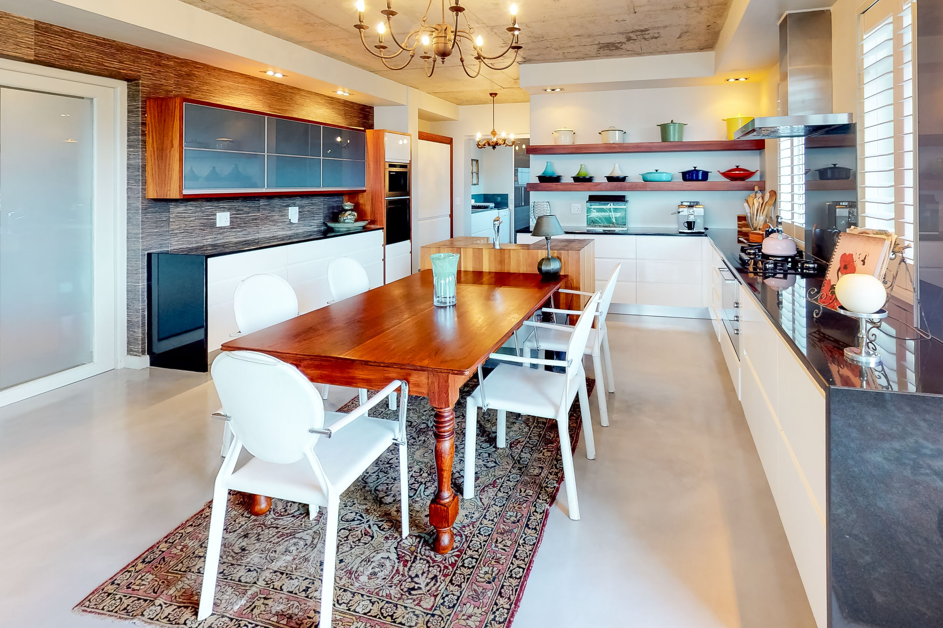 A modern kitchen with a wooden dining table, white chairs, and a patterned rug.