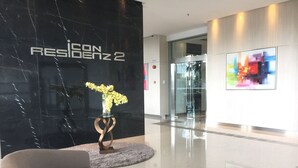 Un hall d’entrée moderne avec un mur en marbre noir, un vase en verre contenant des fleurs jaunes, un canapé gris et une table basse en bois.