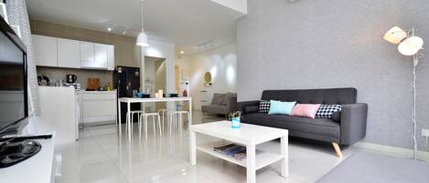A modern living room with a grey sofa, white coffee table, and a kitchen in the background.