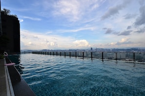 Ein Infinity-Pool mit Blick auf eine Stadtlandschaft, einem Metallgeländer und einem klaren Himmel.
