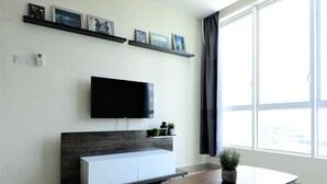 Una sala de estar moderna con un televisor de pantalla plana, un mueble blanco, una mesita con una planta y un ventanal grande.