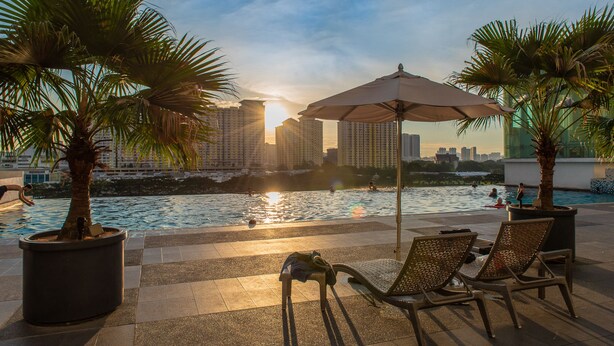 Un área de piscina en la azotea con sillones, sombrillas y palmeras.