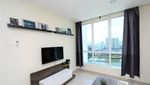 Una sala de estar moderna con un amplio ventanal, un televisor de pantalla plana, una consola blanca y una pequeña planta en maceta.