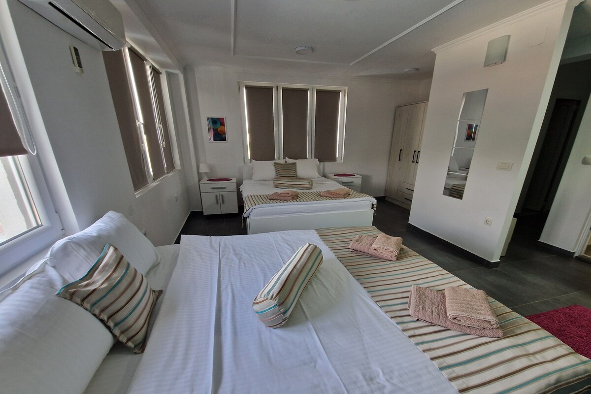 A hotel room with two beds, a small desk, a wardrobe, and a window.
