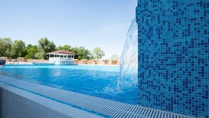 A swimming pool with a waterfall feature, a covered seating area, and a tiled wall. - Flamingo resort (Belgrade)