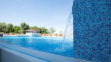 Una piscina con caída de agua, zona de estar techada y pared de azulejos.