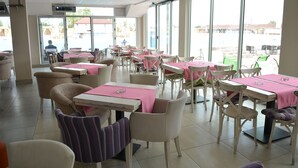 A spacious indoor dining area with tables and chairs, large windows, and a view of the outside. - Flamingo resort (Belgrade)