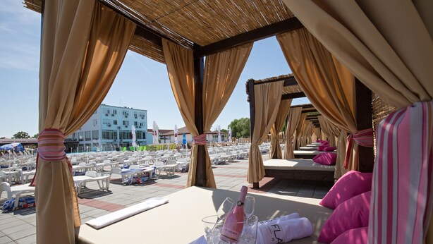 A sunlit outdoor seating area with tables and chairs, a bottle of champagne, and a view of a building in the background. - Flamingo resort (Belgrade)