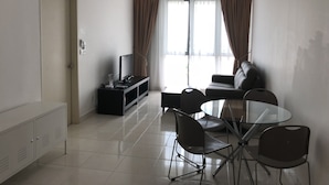 Ein modernes Wohnzimmer mit einem Flachbildfernseher auf einem schwarzen Standfuß, einem Glastisch mit vier Stühlen, einer Couch und einem Deckenventilator.