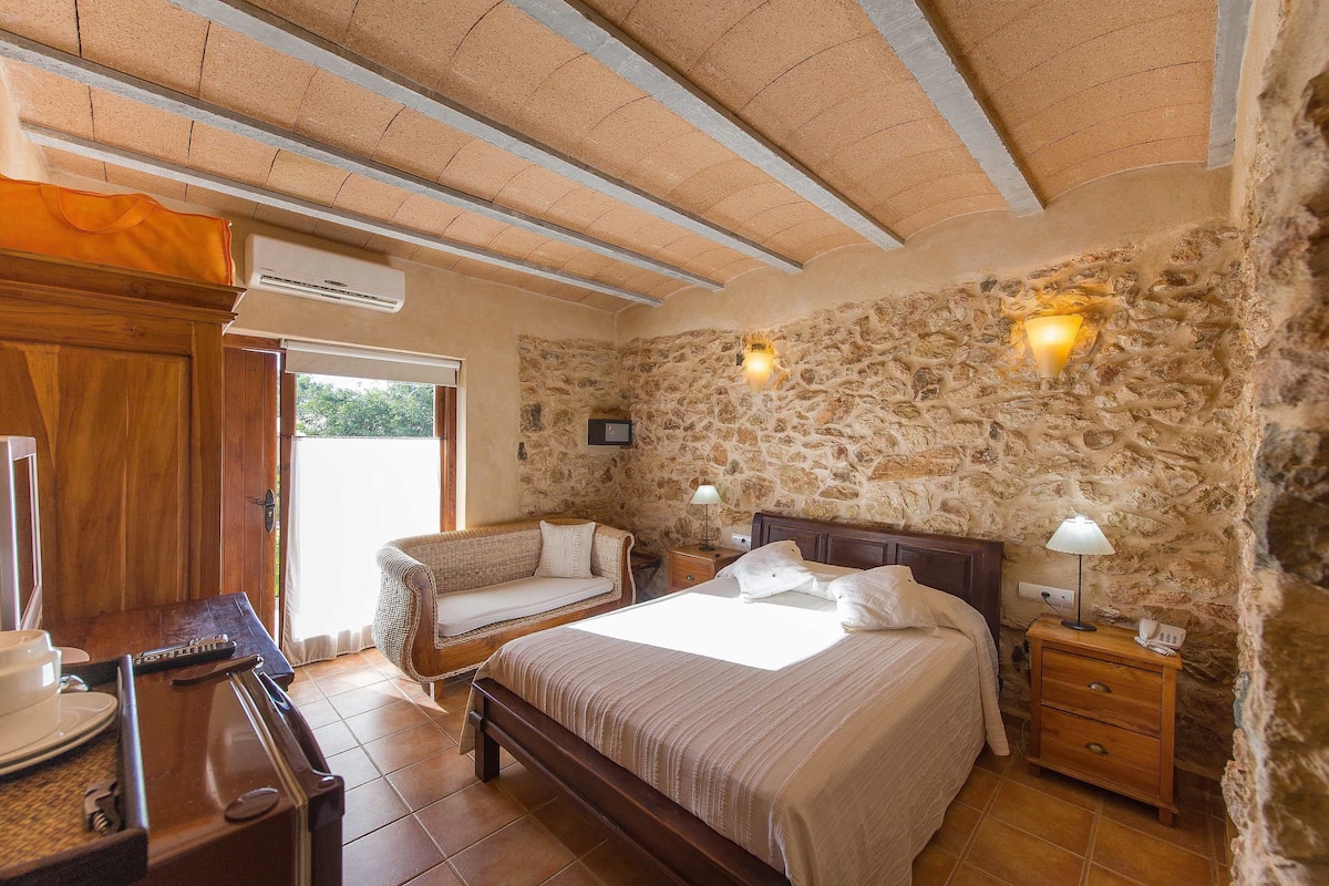 Ein Schlafzimmer mit Steinwand, einem Bett, einem Nachttisch mit Lampe, einer hölzernen Bank und einem Fenster.