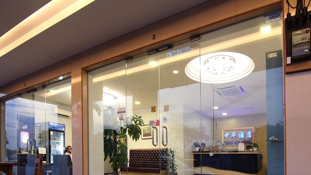 Un hall d'accueil d'hôtel avec une entrée en verre, un comptoir d'accueil et un espace détente comprenant un canapé et des fauteuils.
