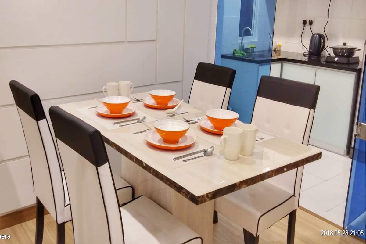 Un coin repas avec une table rectangulaire dressée pour quatre personnes, agrémentée de bols orange et d’assiettes blanches, entourée de chaises à l’habillage noir et blanc.