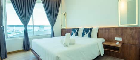 A hotel room with a large bed, a wooden headboard, a bedside table, a mirror, and a view of the city through the window.
