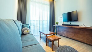 A modern living room with a sofa, a wooden coffee table, a television, and a dining area with a wooden counter. - The Wave by ExcluSuites Malacca (Malacca City)