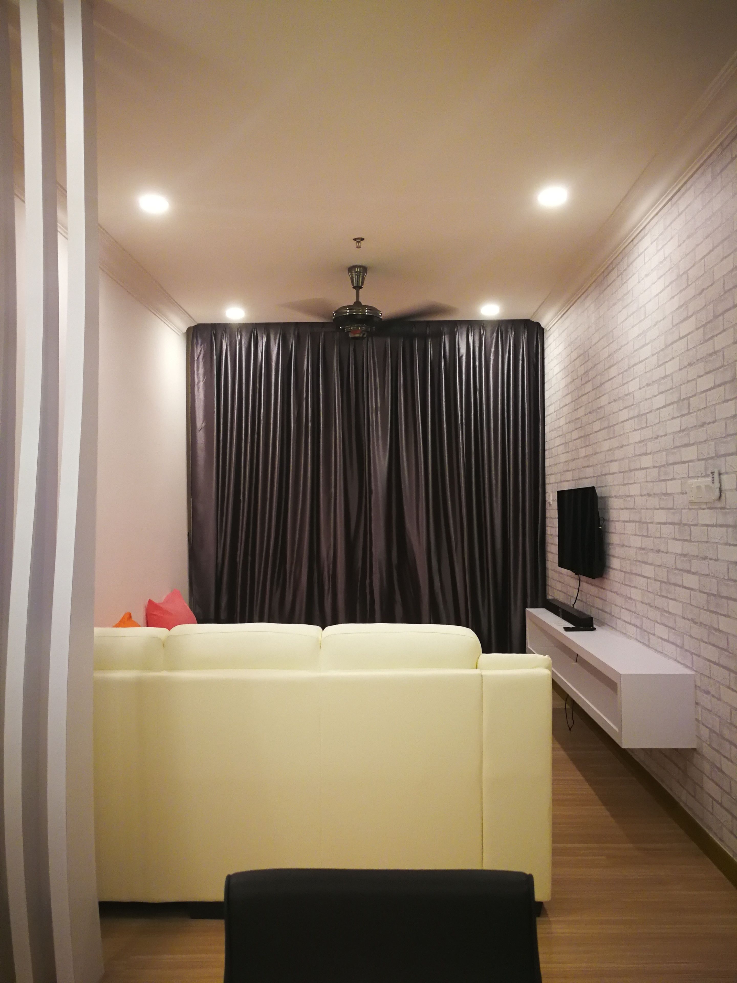 Sala de estar com sofá branco, poltrona preta, painel branco para entretenimento e televisão preta em uma parede com textura de tijolos.