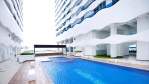 A modern hotel with a large indoor swimming pool, multiple balconies, and a view of the ocean. - The Wave by ExcluSuites Malacca (Malacca City)