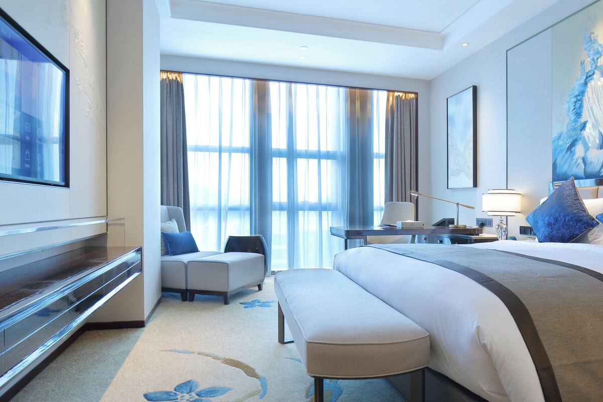 Habitación de hotel moderna con una cama grande, un escritorio, una silla y un ventanal con cortinas.