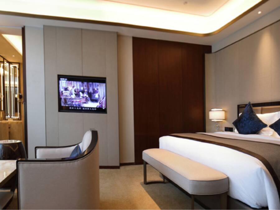 A hotel room with a bed, a desk, a chair, a TV, and a bedside table.