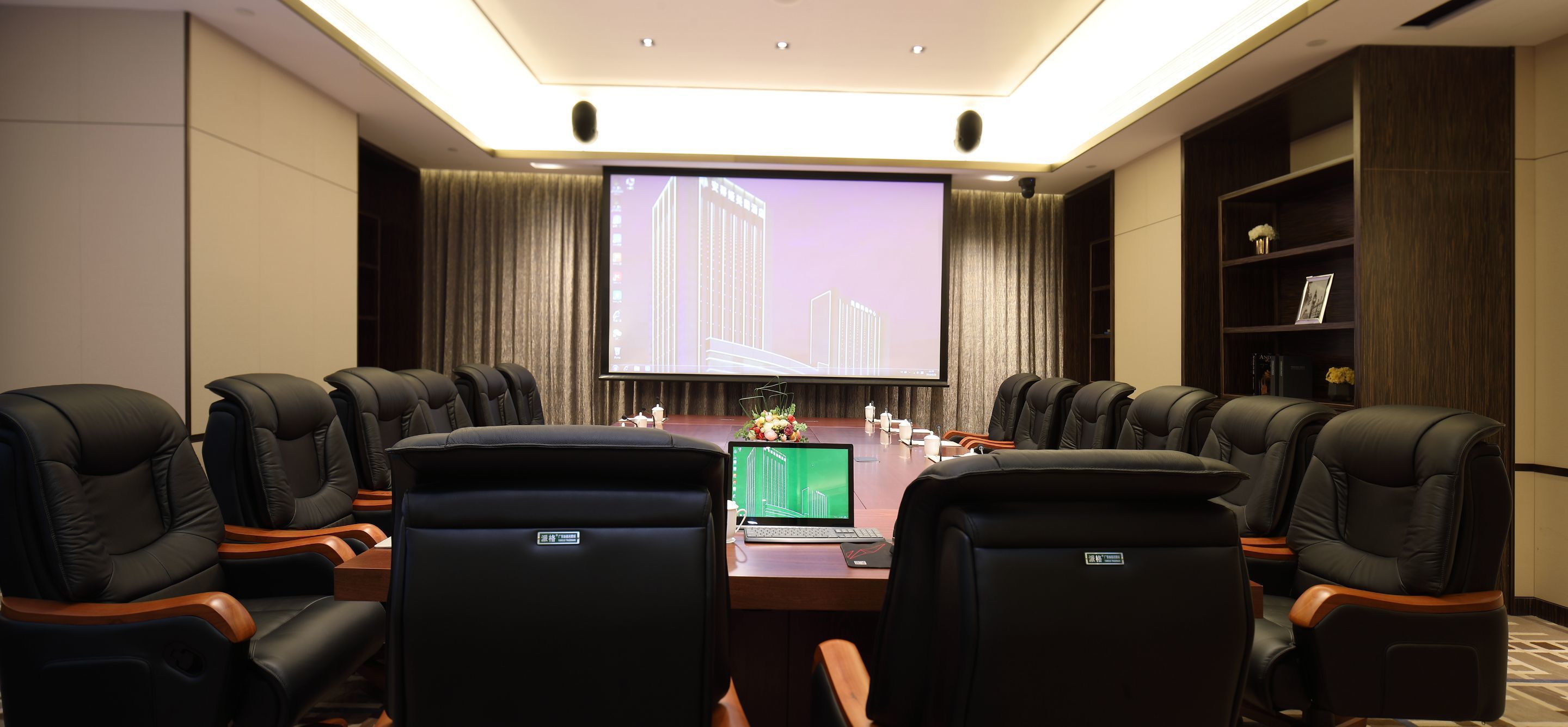 A conference room with a large screen, a laptop, and a table with chairs.