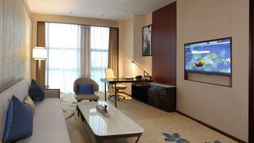 A hotel room with a sofa, a desk, a chair, a TV, and a large window with curtains.