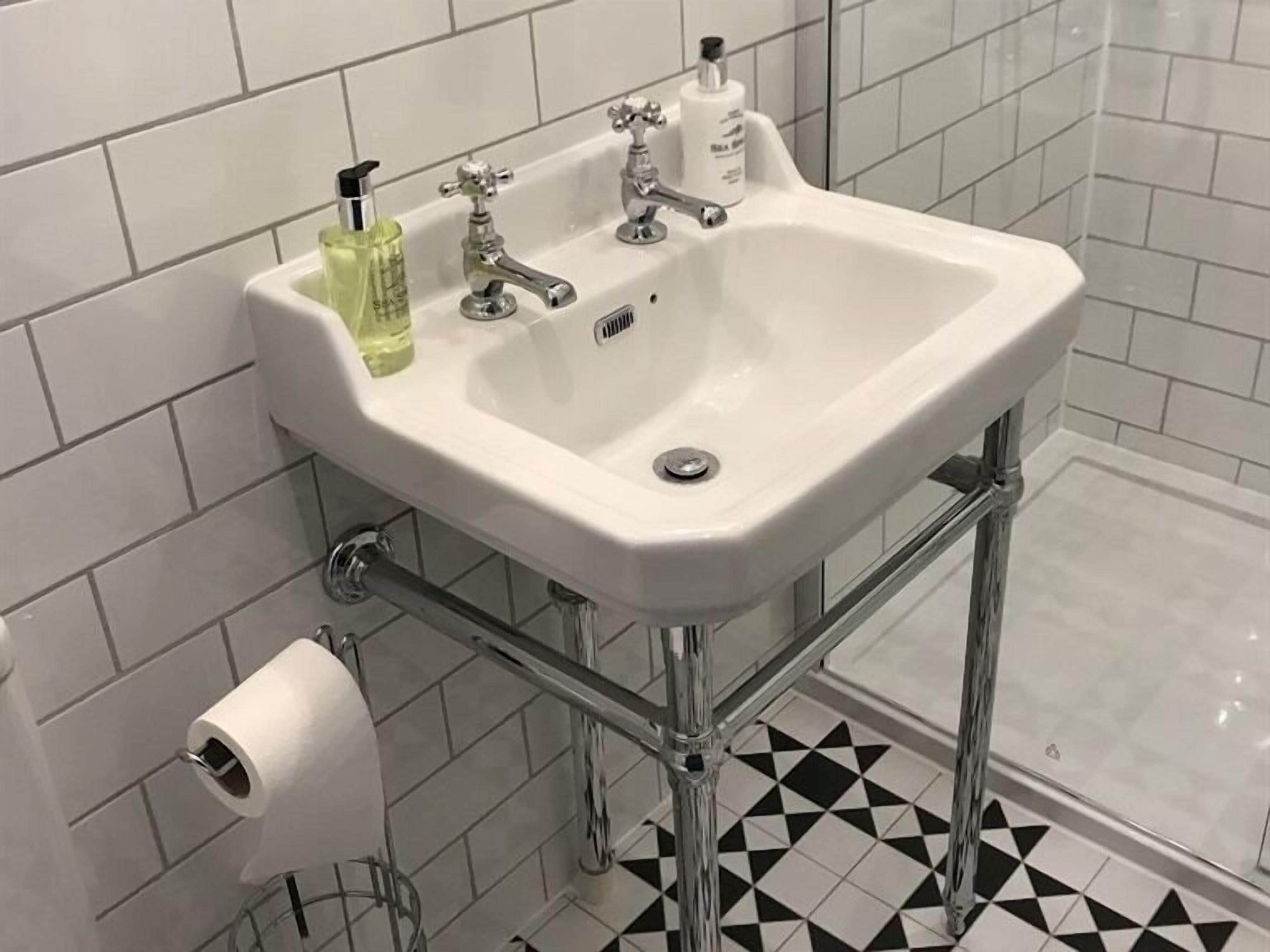 A bathroom with a white sink, two faucets, a toilet paper holder, and a shower area.