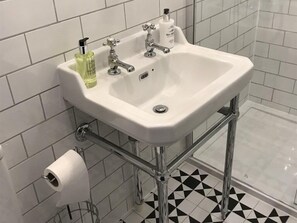 A bathroom with a white sink, two faucets, a toilet paper holder, and a shower area.
