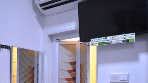 A narrow hallway with a white wall, a door with a geometric patterned glass panel, and a mounted air conditioning unit above. - dr96inn (Kuantan)