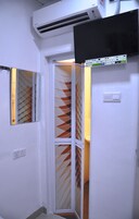 Un pasillo estrecho con pared blanca, una puerta con un panel de vidrio de diseño geométrico y una unidad de aire acondicionado instalada arriba.
