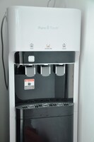Dispensador de agua con opciones de agua caliente, alcalina y fría, y una etiqueta de advertencia.