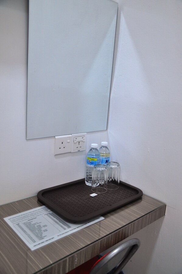 Une petite chambre d’hôtel avec un miroir, un plateau contenant des bouteilles d’eau et des verres, et un document posé sur le comptoir.