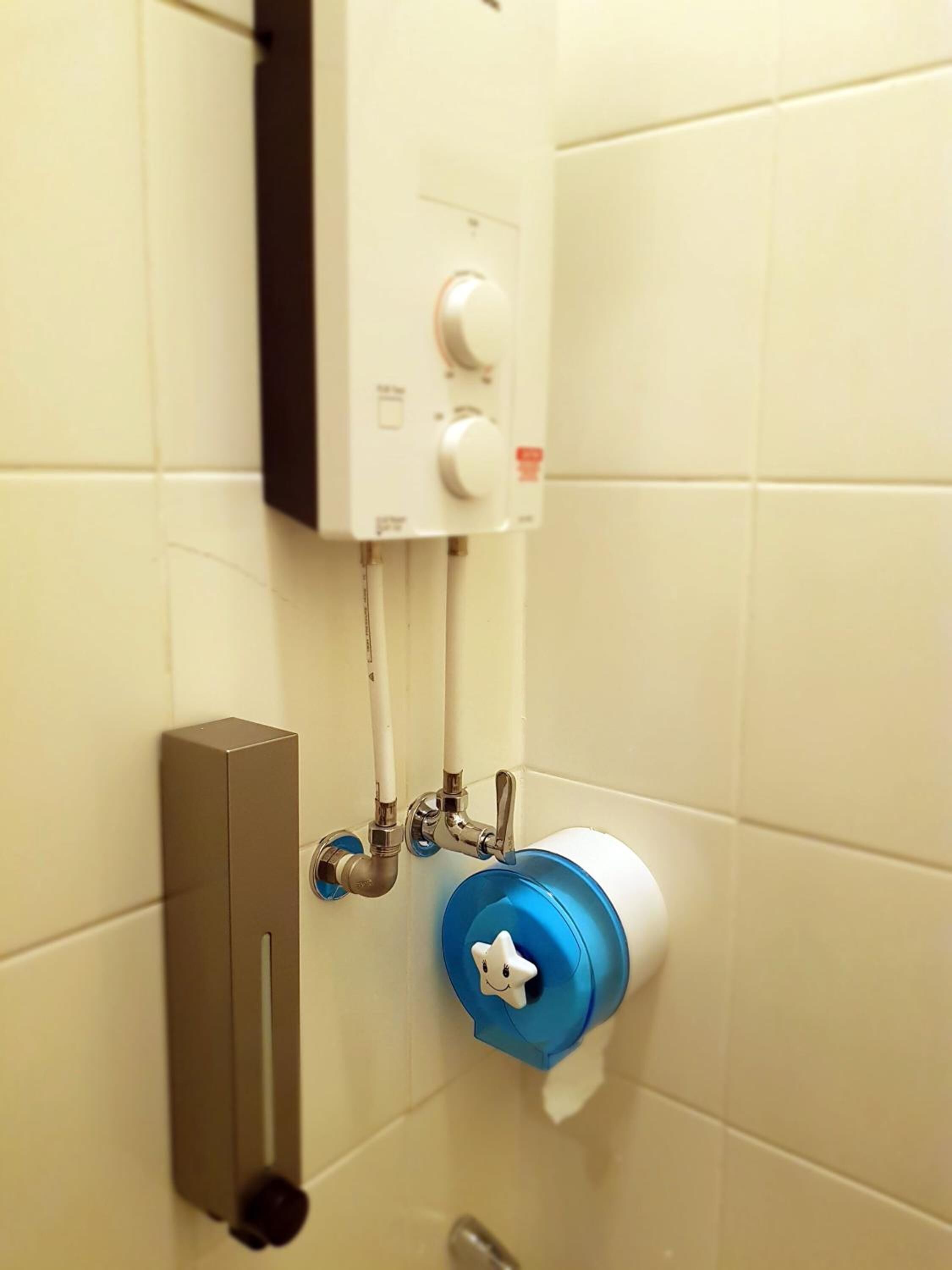 A bathroom with a toilet, a hand dryer, and a wall-mounted heater.