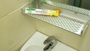 A bathroom sink with a mirror above it, a toothbrush holder with a toothbrush, and a small vase with flowers. - dr96inn (Kuantan)