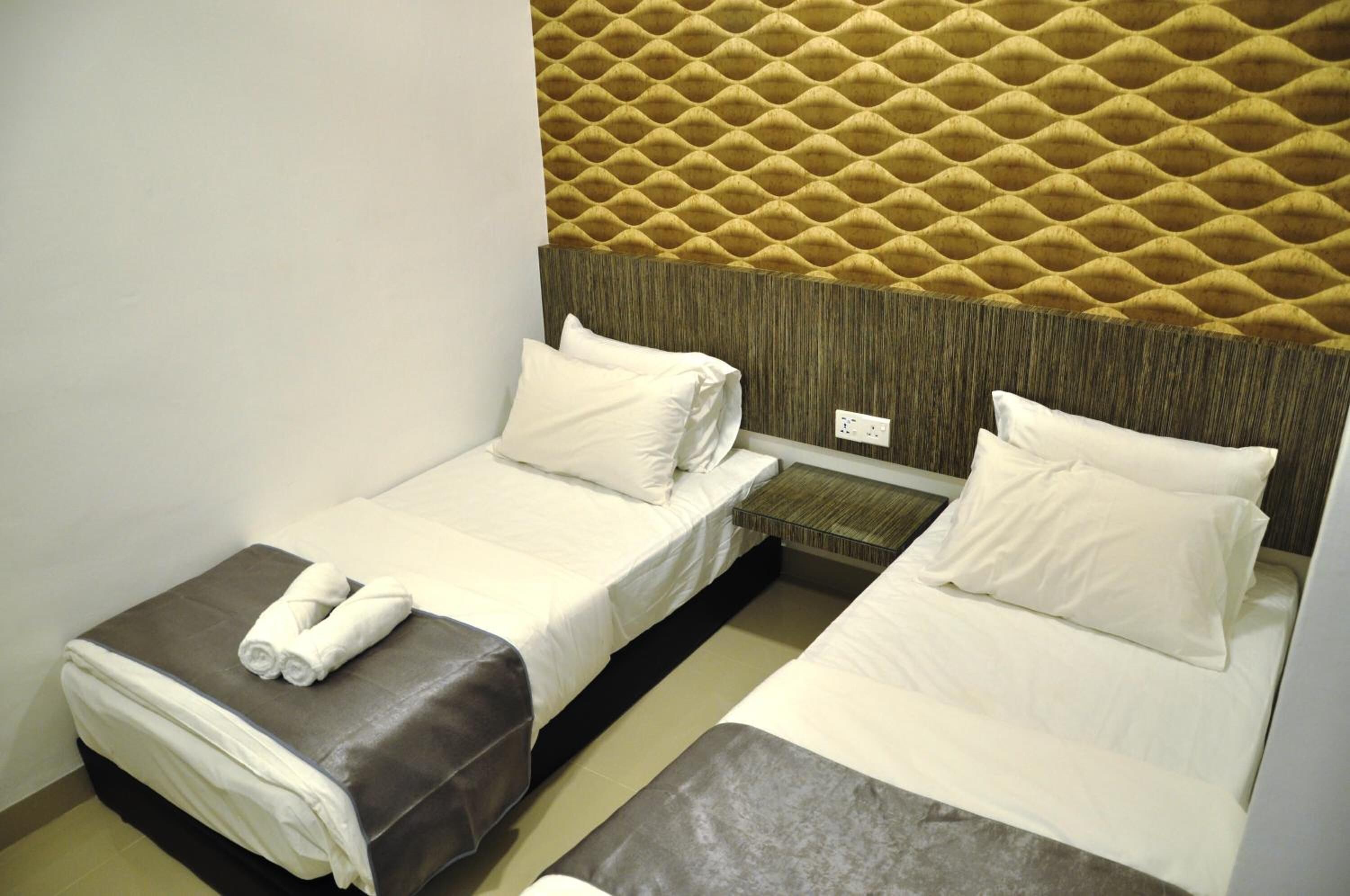 Una habitación de hotel con dos camas individuales, cabecera de madera y una mesita de noche pequeña.