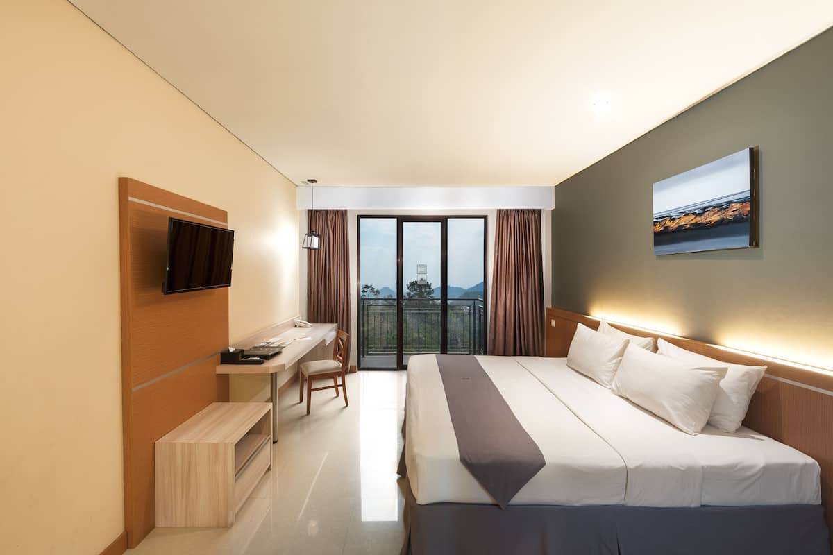 A hotel room with a bed, desk, chair, TV, and a balcony with curtains.