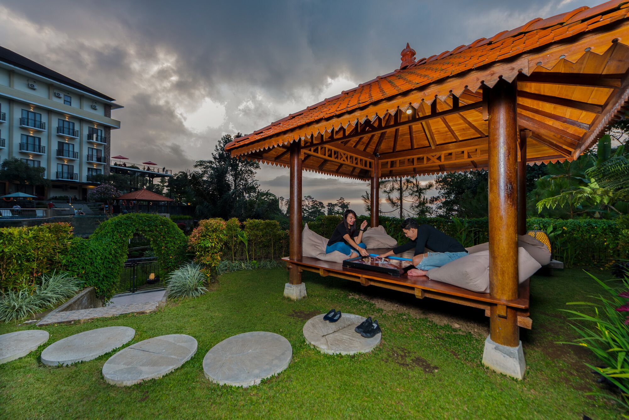 A wooden gazebo with a thatched roof, surrounded by a well-maintained garden with stone pathways and lush greenery.