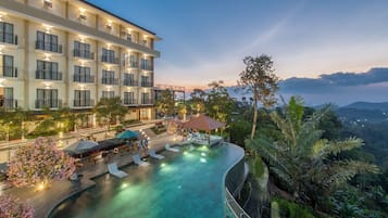 A hotel with a swimming pool, outdoor seating, and a view of the surrounding landscape.