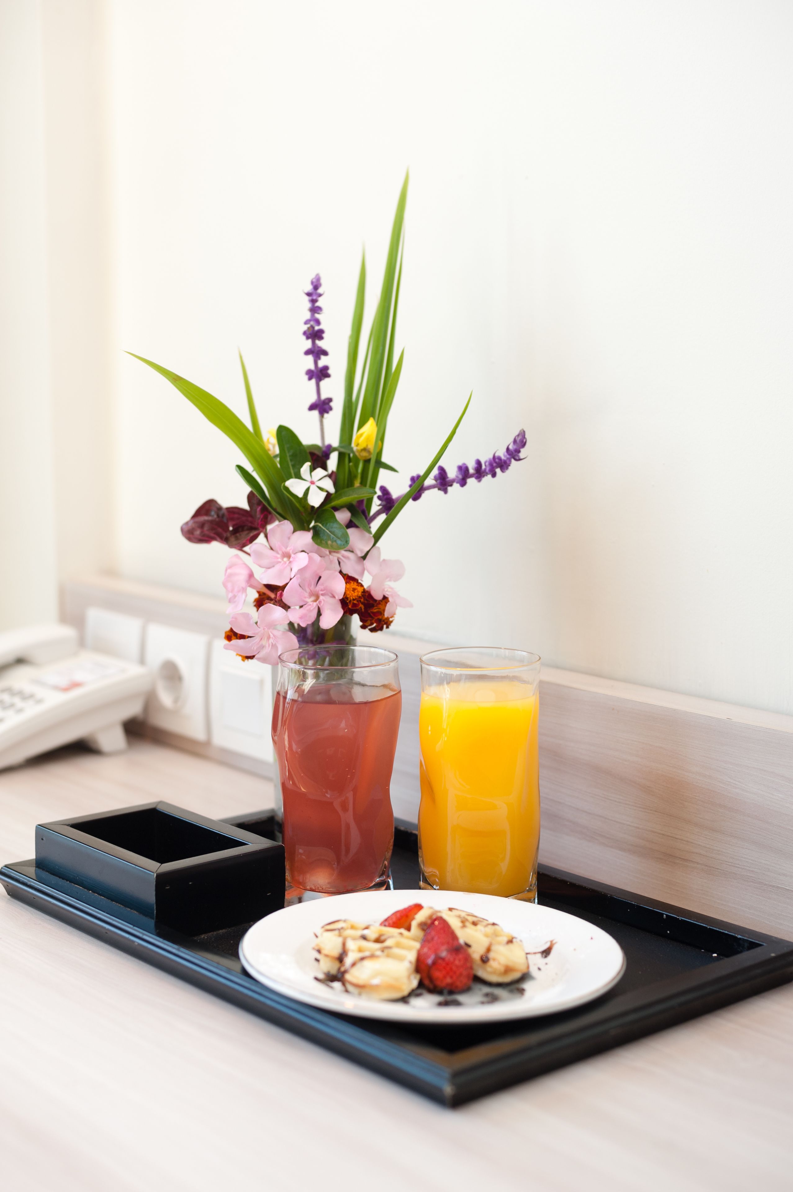 A tray with a plate of food, a glass of juice, and a vase of flowers.