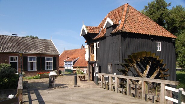 A wooden bridge leading to a traditional building with a watermill. - Hotel Restaurant 'T Holt (Diepenheim)