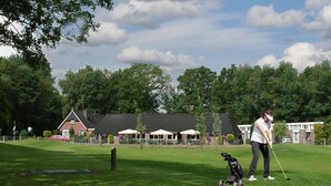 A golf course with a clubhouse, a stroller, and a person preparing to play. - Hotel Restaurant 'T Holt (Diepenheim)