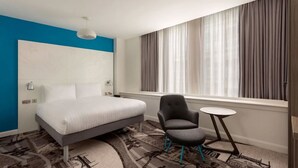 A modern hotel room with a bed, a chair, a small table, and a large window with curtains. - Ibis Styles Glasgow Central (Glasgow)
