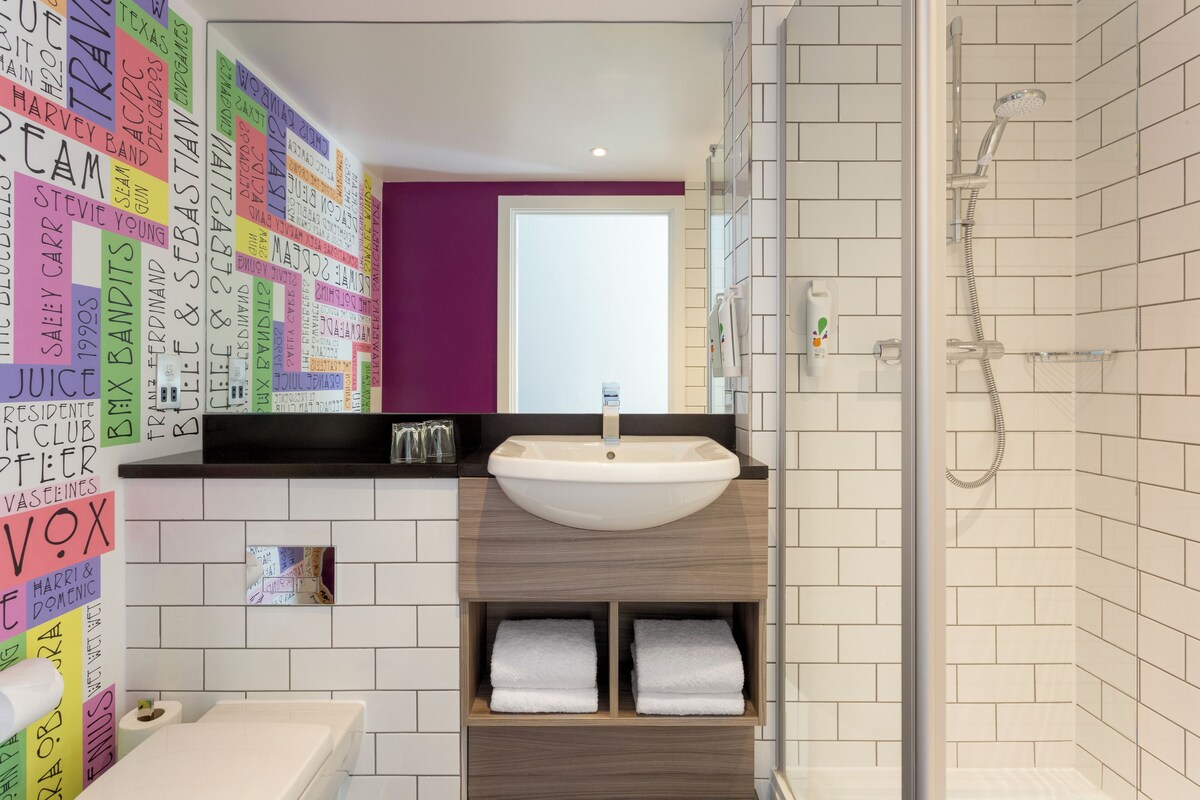A modern bathroom with a white sink, a shower, and a wall covered with colorful sticky notes.