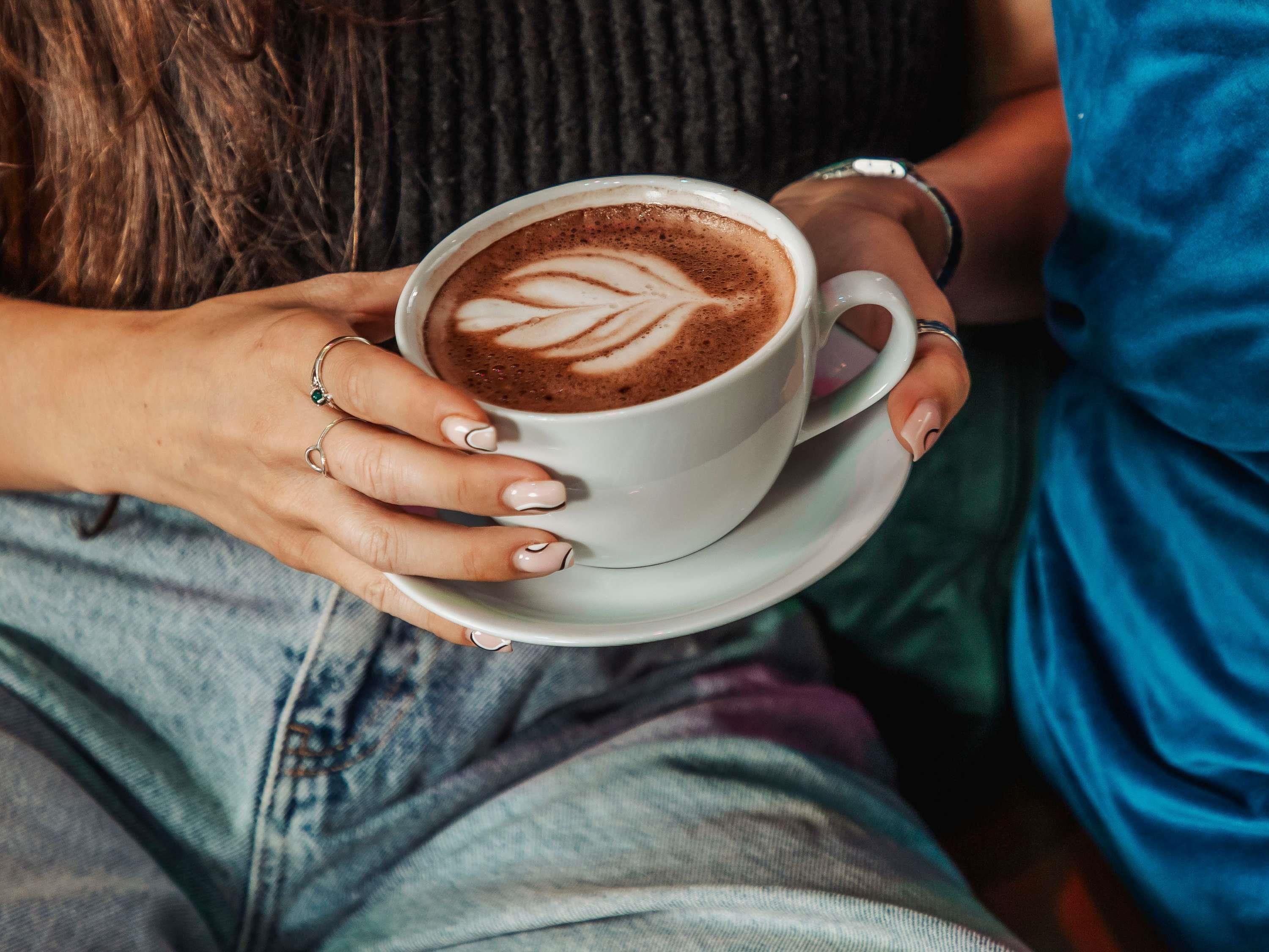 Une personne tenant une tasse de café ornée d’un motif en latte art.
