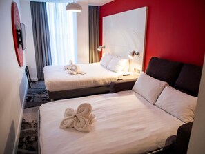 A hotel room with two beds, a red accent wall, a large abstract artwork, and a view of the outdoors. - Ibis Styles Glasgow Central (Glasgow)