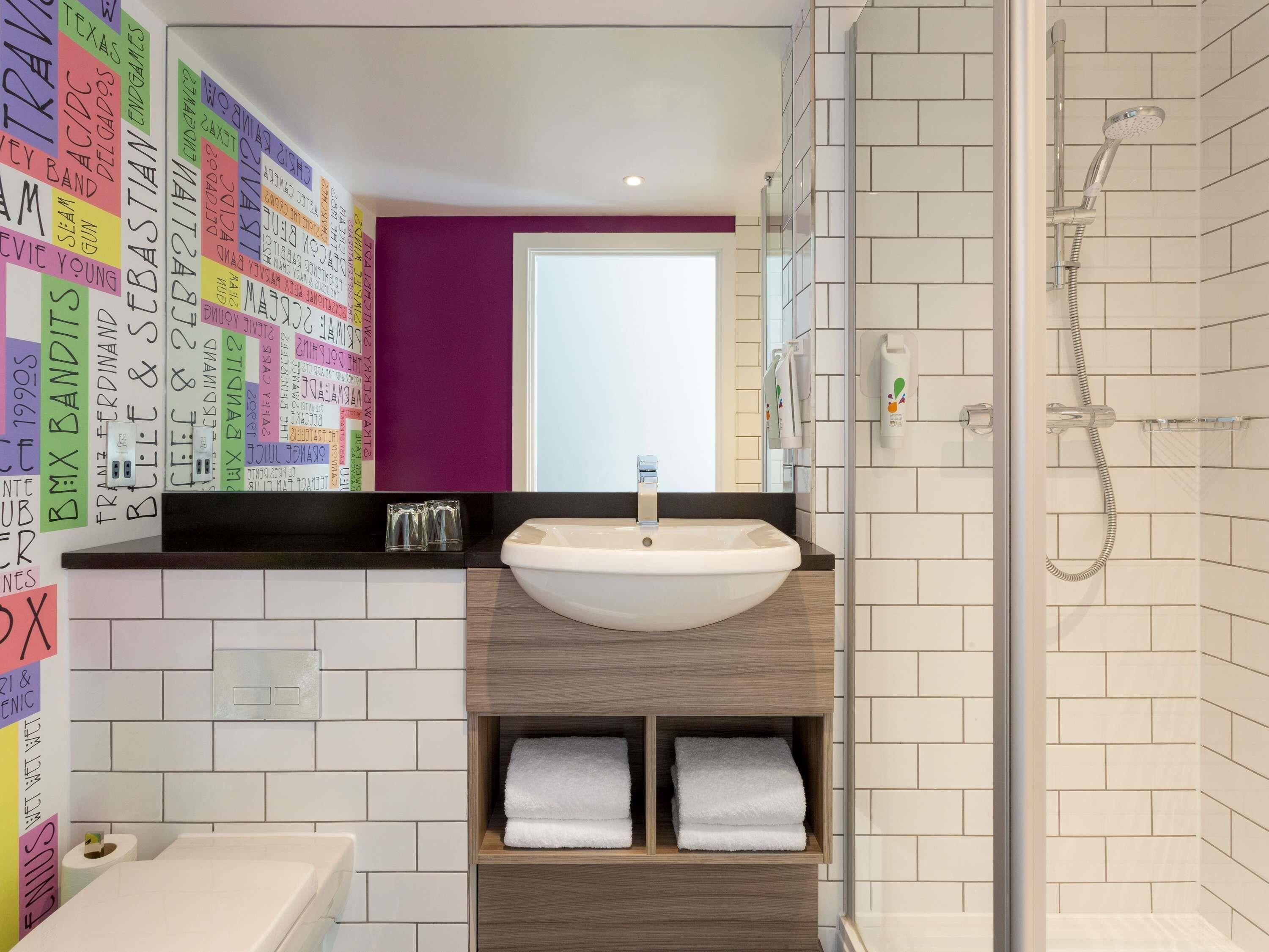 A modern bathroom with a white sink, a shower, and a purple accent wall.