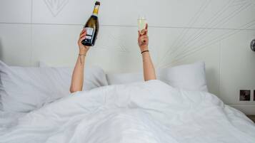 A person holding a bottle and a glass in a bed with white bedding and a geometric wall design.