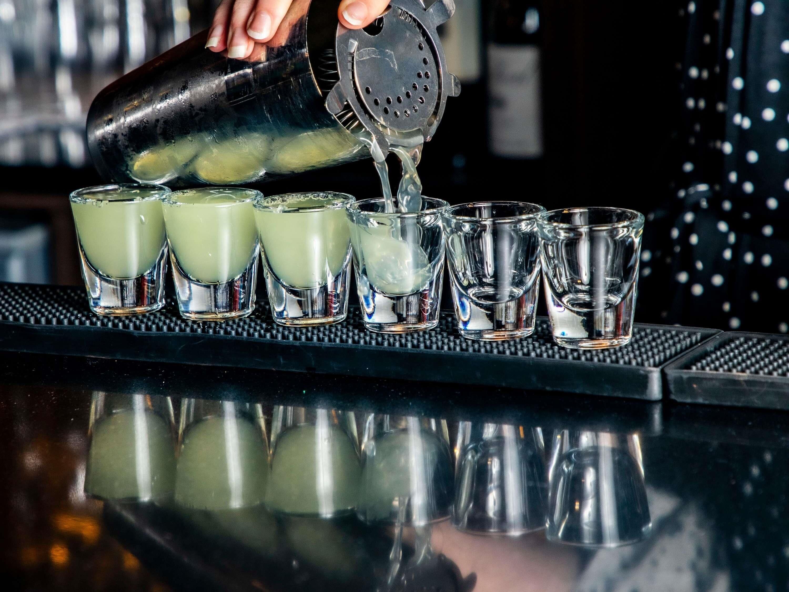 A bartender pouring a drink into shot glasses on a bar counter.